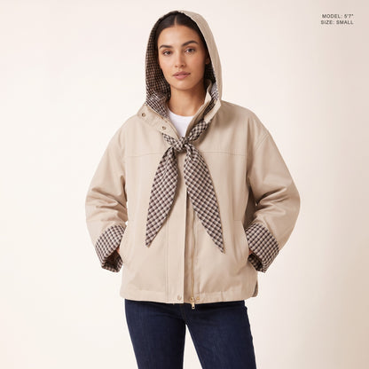 The Hartley Hooded Windbreaker in Beige, hood up with the plaid scarf tied at the throat, model 5 foot 7 wearing size Small