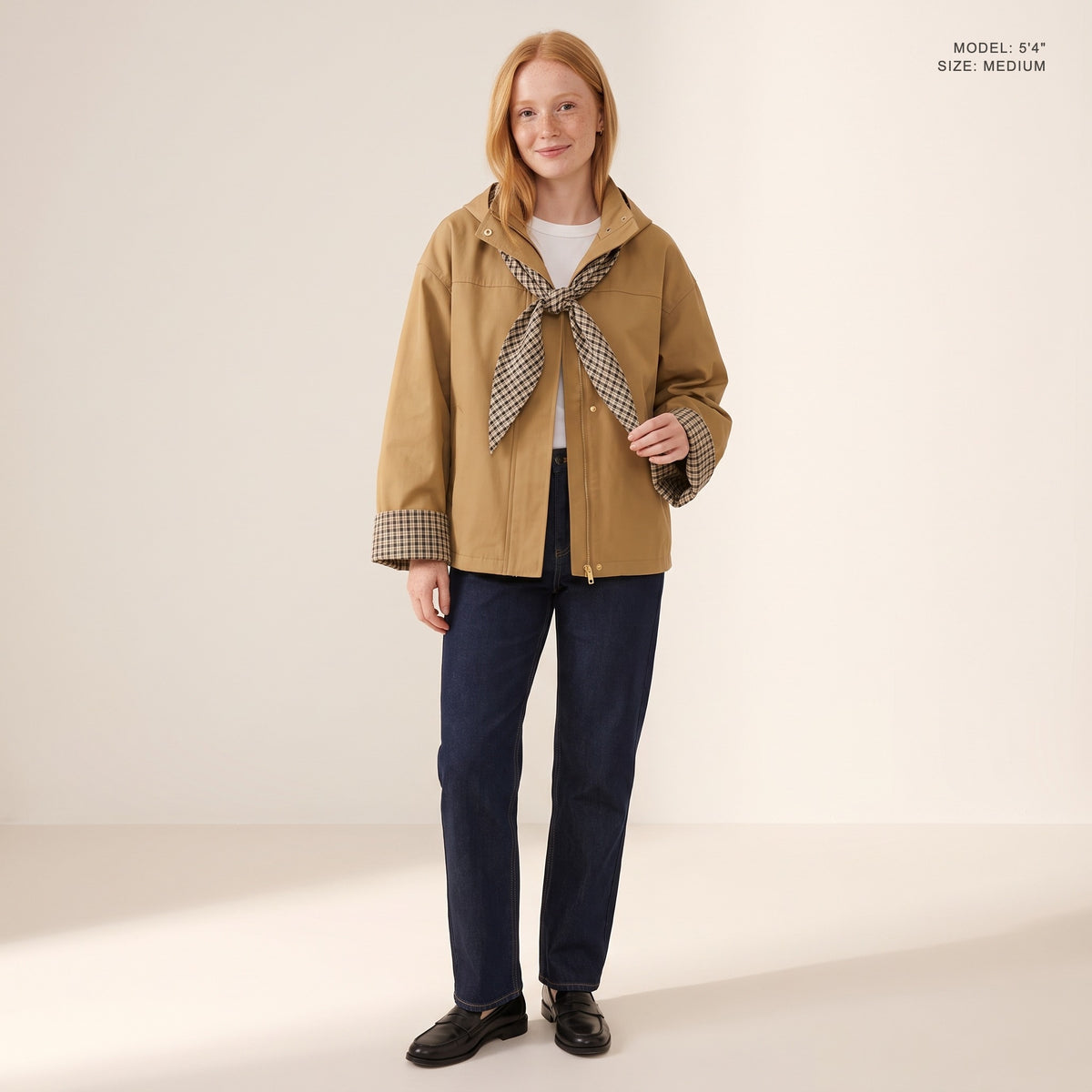 The Hartley Hooded Windbreaker in Khaki with the plaid scarf knotted at the collar, model 5 foot 4 wearing size Medium