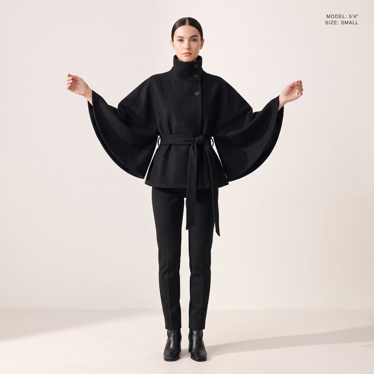 The Marlowe Cape Coat in Black, front view with the cape sleeves spread, model 5 foot 4 wearing size Small
